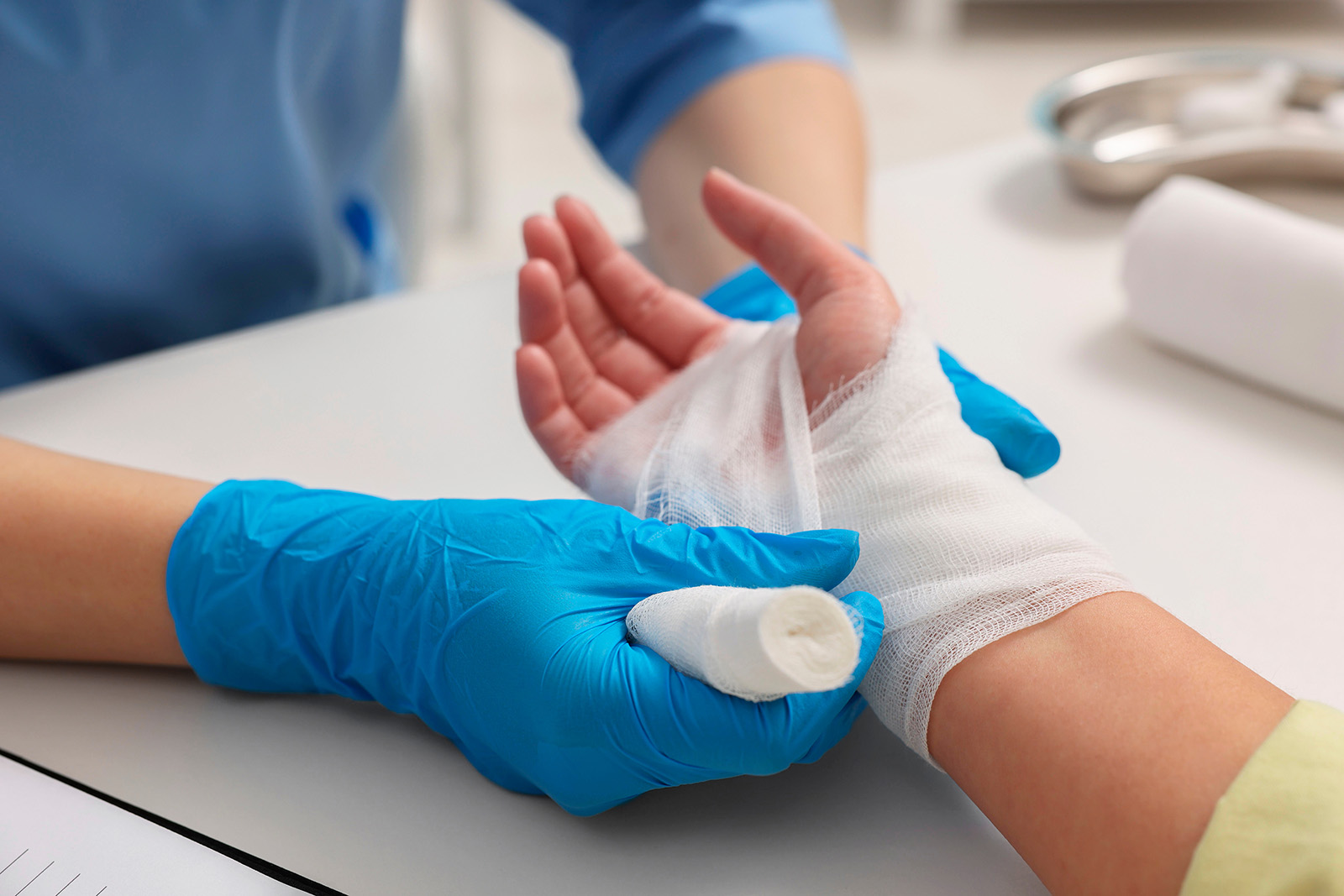 Image of a health care provider with gloves on bandaging a patient's hand and wrist.